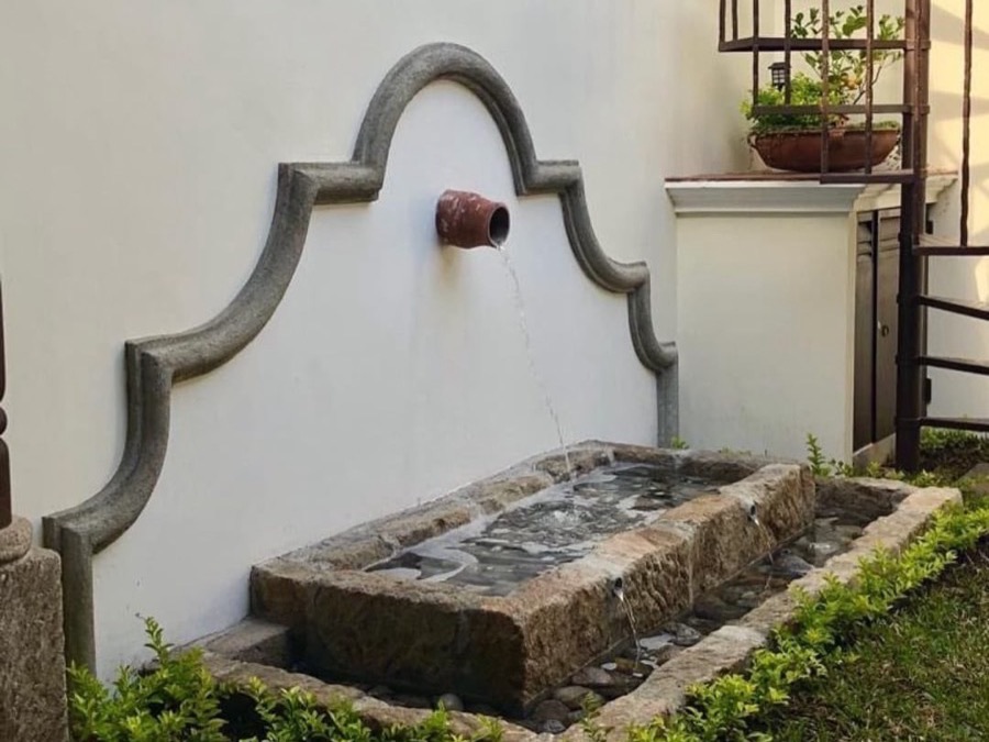 Fuente de piedra colonial en un jardín de una obra de BR Constructora